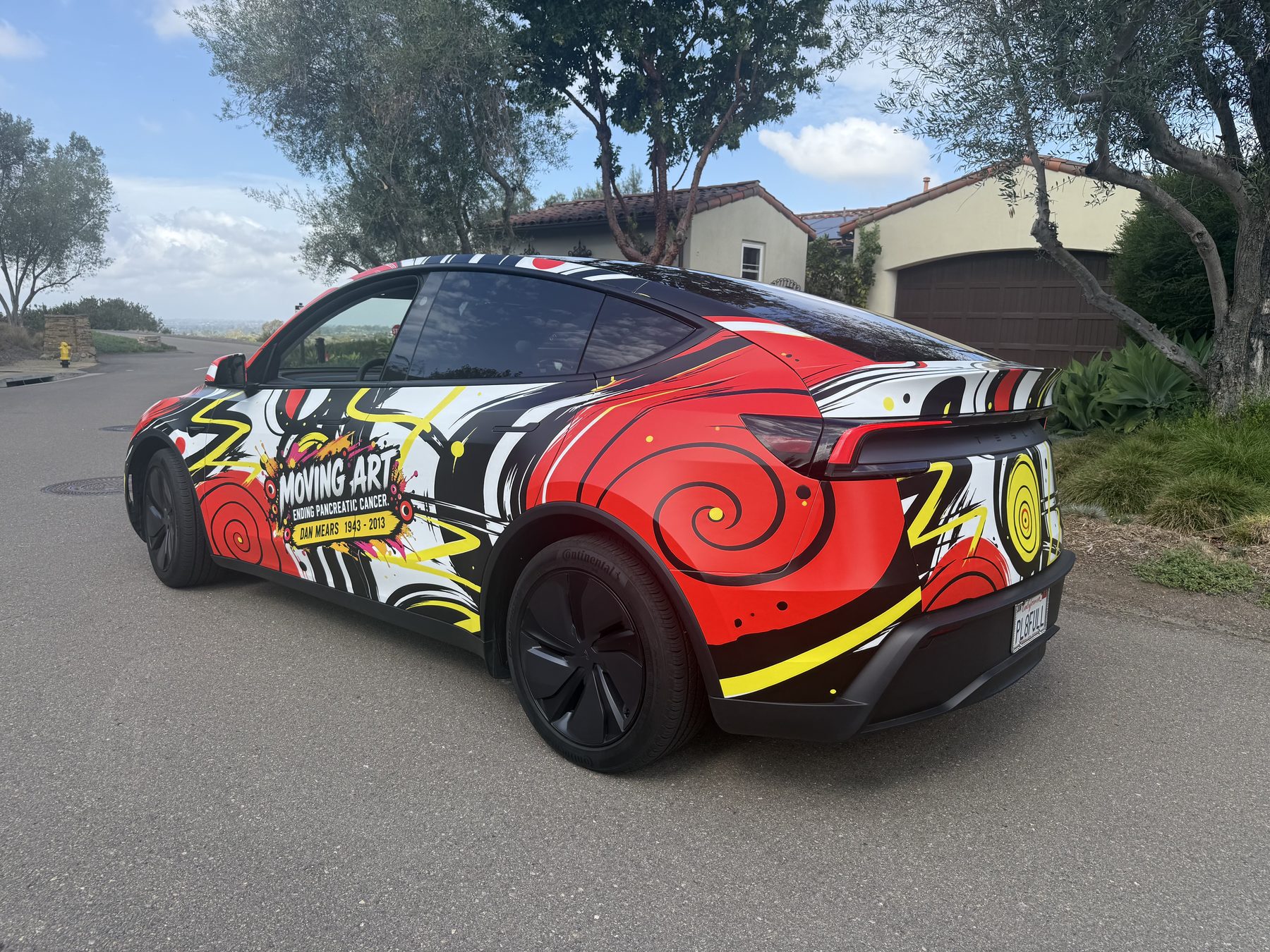 Rear three-quarter view of the Moving Art wrapped Tesla parked on a coastal street