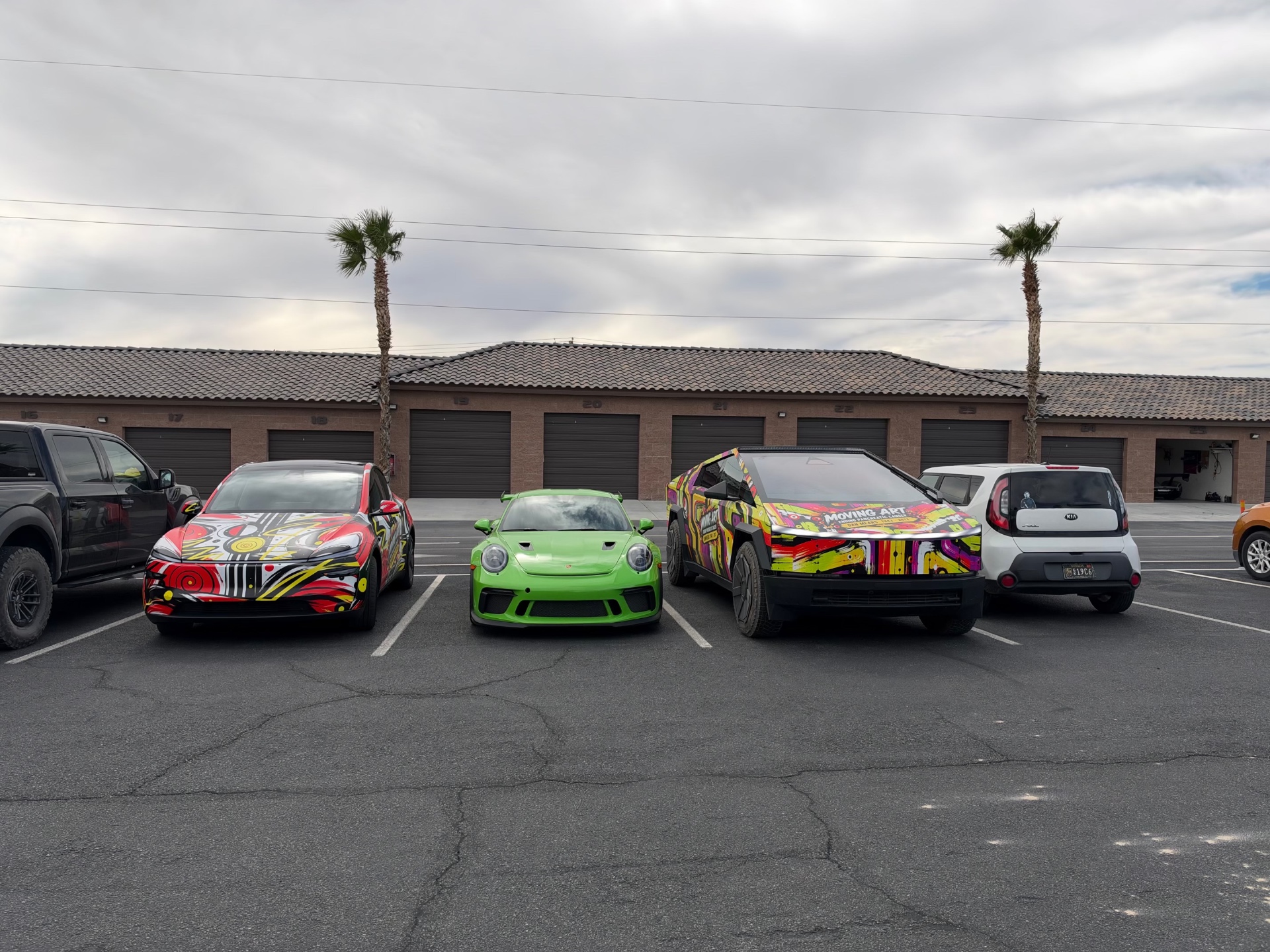 Wrapped Tesla and Cybertruck parked alongside a green Porsche and a compact car
