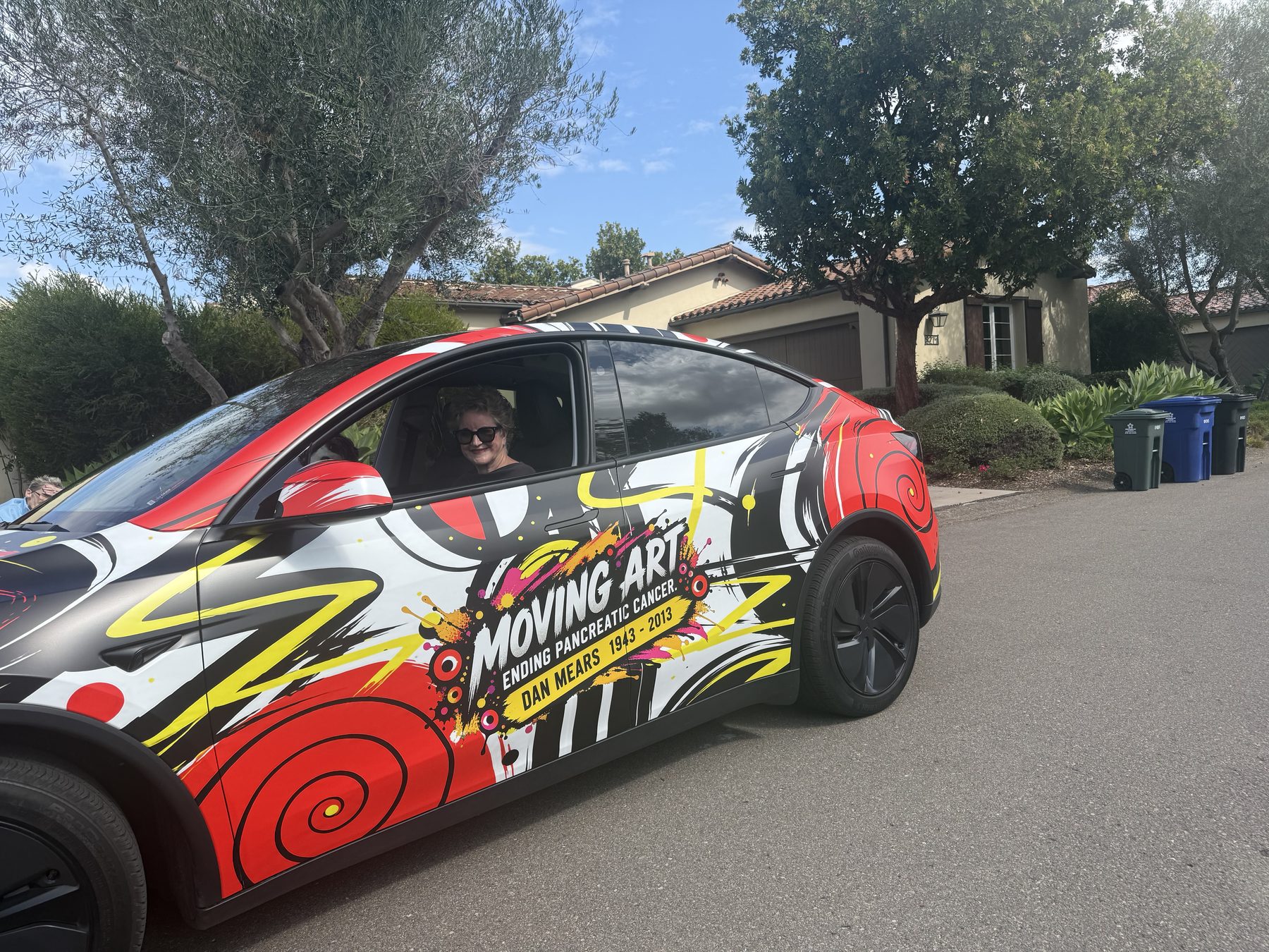 The Moving Art wrapped Tesla driving down a tree-lined street