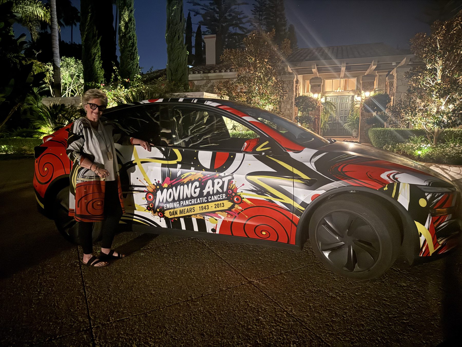 Susan Fielder standing with the wrapped Tesla at night outside a lit home