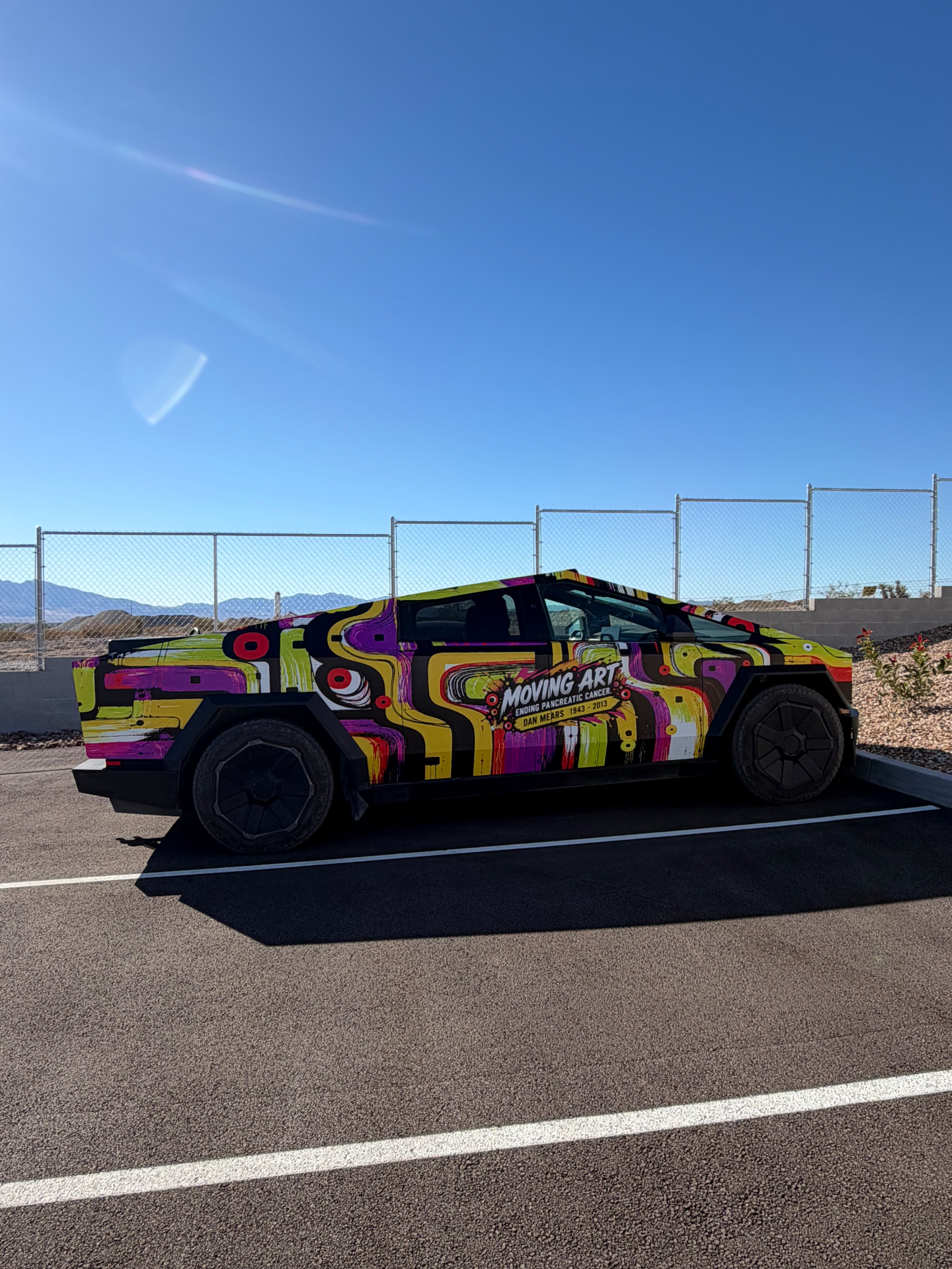 Side view of a Cybertruck in daylight with yellow, pink, purple and black Moving Art wrap
